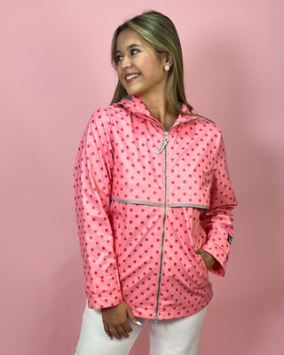 Woman wearing a pink polka dot raincoat against a pink background