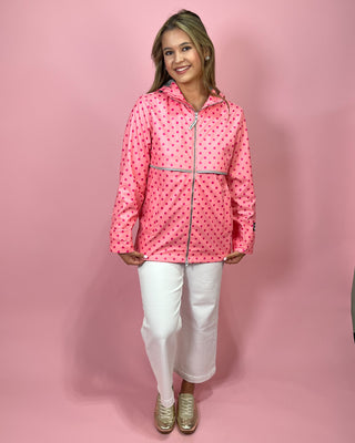 Person wearing a pink raincoat with white polka dots on a pink background