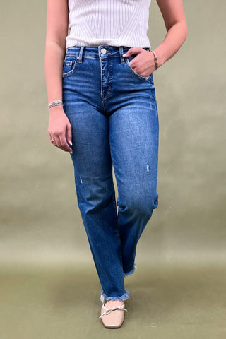 Person wearing blue jeans and a white top on a plain background