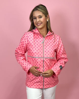 Woman wearing a pink polka dot raincoat against a pink background