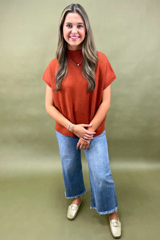 Rust orange knit cap sleeve sweater paired with light wash wide leg frayed hem jeans and gold loafers