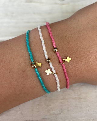Three colorful bracelets with gold charms on a wrist against a neutral background