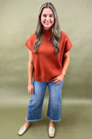 Rust orange knit cap sleeve sweater paired with light wash wide leg frayed hem jeans and gold loafers