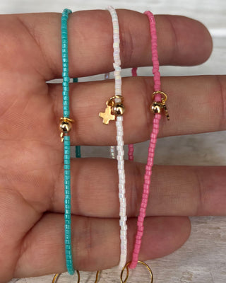 Three beaded bracelets on a hand with gold charms against a neutral background