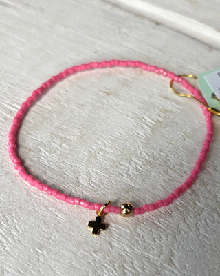Pink beaded bracelet with a black and gold charm on a light wooden surface