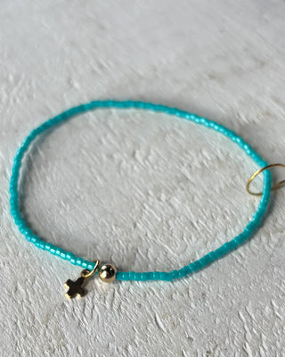 Turquoise beaded bracelet with a gold charm on a light gray background