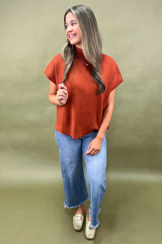 Rust orange knit cap sleeve sweater paired with light wash wide leg frayed hem jeans and gold loafers