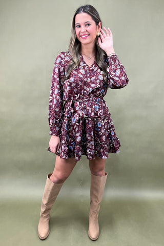 Woman wearing a floral dress with long sleeves and beige knee-high boots on a green background