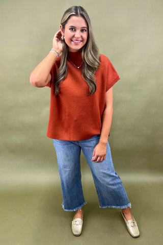 Rust orange knit cap sleeve sweater paired with light wash wide leg frayed hem jeans and gold loafers