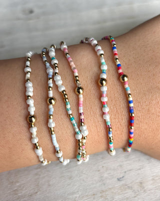 Multicolored beaded bracelets on a wrist against a neutral background