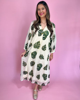 Woman wearing a white dress with green leaf patterns against a pink background