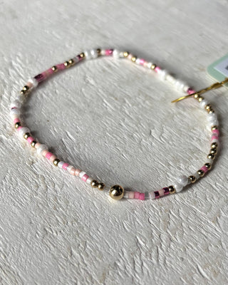 Beaded bracelet with pink, gold, and black beads on a light gray background