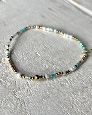 Beaded bracelet with gold, silver, and turquoise beads on a light gray background