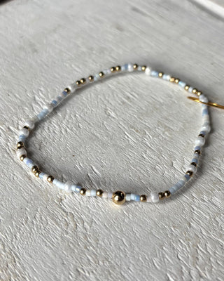 Beaded bracelet with gold and white beads on a light gray surface