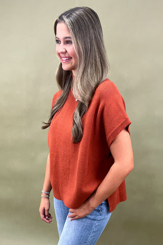 Rust orange knit cap sleeve sweater paired with light wash wide leg frayed hem jeans and gold loafers