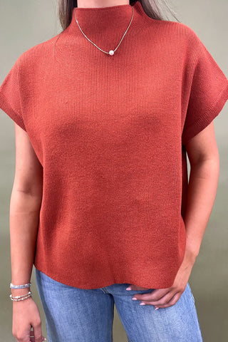 Rust orange knit cap sleeve sweater paired with light wash wide leg frayed hem jeans and gold loafers