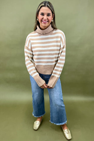 Beige and white striped turtleneck sweater paired with light wash wide leg frayed hem jeans and gold loafers.