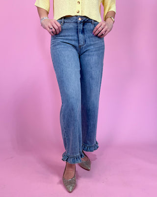 Person wearing blue jeans with ruffled cuffs against a pink background