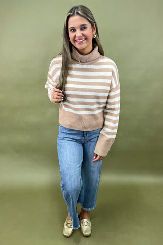 Beige and white striped turtleneck sweater paired with light wash wide leg frayed hem jeans and gold loafers.