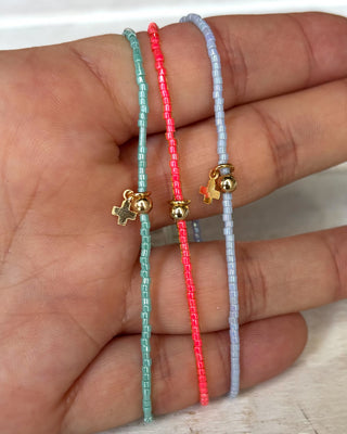 Three beaded bracelets with gold charms on a hand against a neutral background