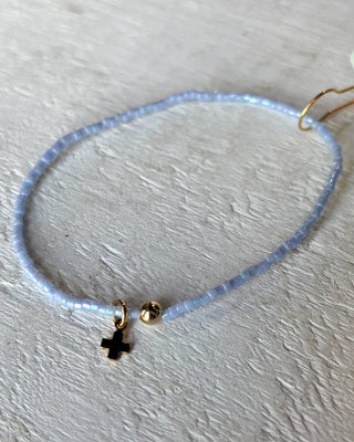 Delicate bracelet with a small cross charm on a light background