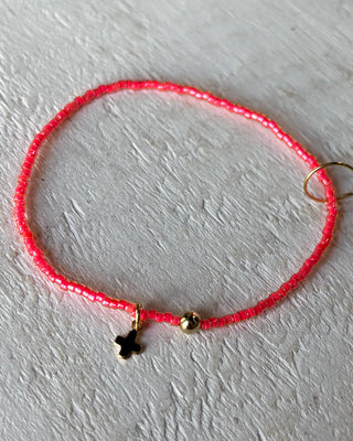 Pink beaded bracelet with gold charm on a white surface