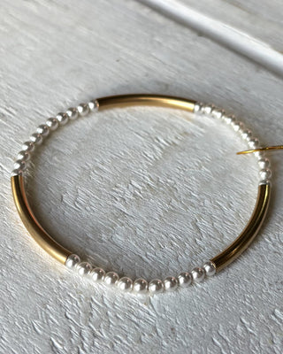 Gold hoop earring with pearl beads on a light gray surface