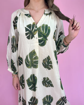 Woman wearing a white dress with green leaf patterns against a pink background