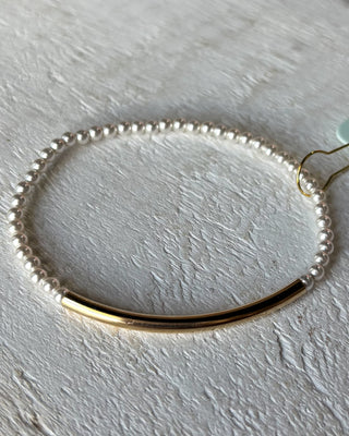 Bracelet with gold bar and pearl-like beads on a light gray background