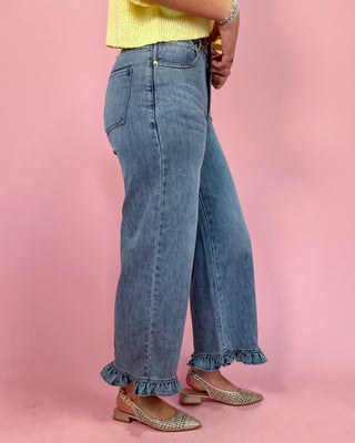 Person wearing blue jeans with ruffled cuffs on a pink background