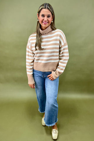 Beige and white striped turtleneck sweater paired with light wash wide leg frayed hem jeans and gold loafers.