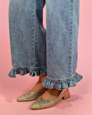 Denim jeans with ruffled cuffs and gold flats on a pink background
