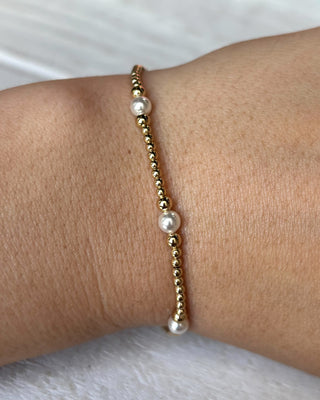 Gold bracelet with pearls on a wrist against a white background