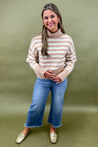Beige and white striped turtleneck sweater paired with light wash wide leg frayed hem jeans and gold loafers.