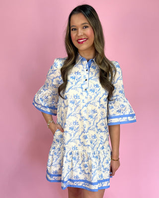 Woman wearing a blue and white floral dress against a pink background