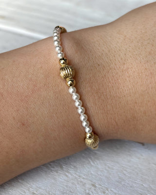 Pearl bracelet with gold accents on a wrist against a neutral background