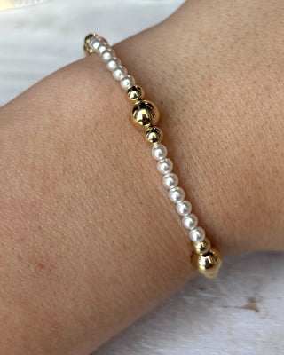 Bracelet with gold and pearl beads on a wrist against a white background