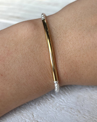 Gold bangle on a wrist with a white background
