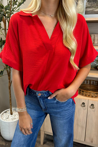 Person wearing a red blouse and blue jeans indoors
