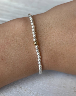 Pearl bracelet with a gold bead on a wrist against a neutral background