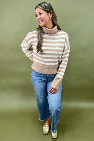 Beige and white striped turtleneck sweater paired with light wash wide leg frayed hem jeans and gold loafers.