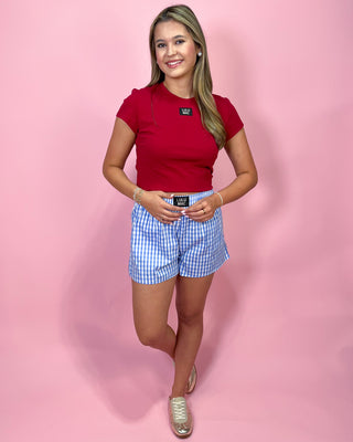 Woman wearing a red top and blue checkered shorts on a pink background