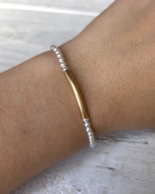 Bracelet with gold bar and silver beads on a wrist against a light background