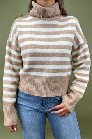 Beige and white striped turtleneck sweater paired with light wash wide leg frayed hem jeans and gold loafers.
