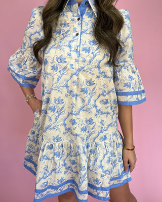 Woman wearing a blue and white floral dress against a pink background