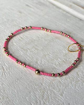 Pink beaded necklace with gold beads on a light wooden surface