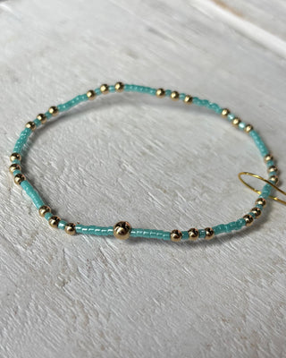 Turquoise beaded bracelet with gold beads on a light wooden surface