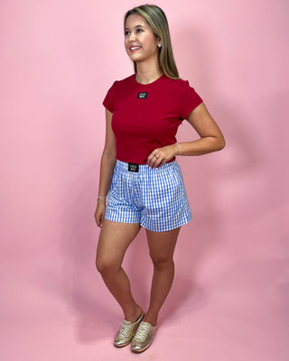 Woman wearing a red top and blue checkered shorts on a pink background