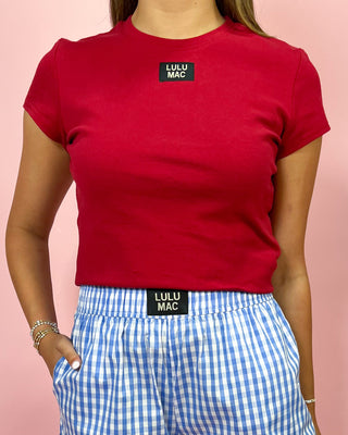 Person wearing a red t-shirt and blue checkered shorts with LULU MAC branding on a pink background