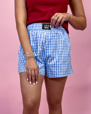 Person wearing blue checkered shorts with a visible brand label on a pink background